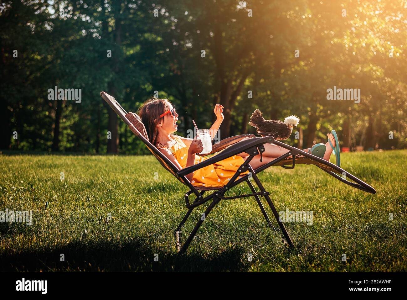 Happy girl sitting in the garden with a chicken on her chair Stock Photo