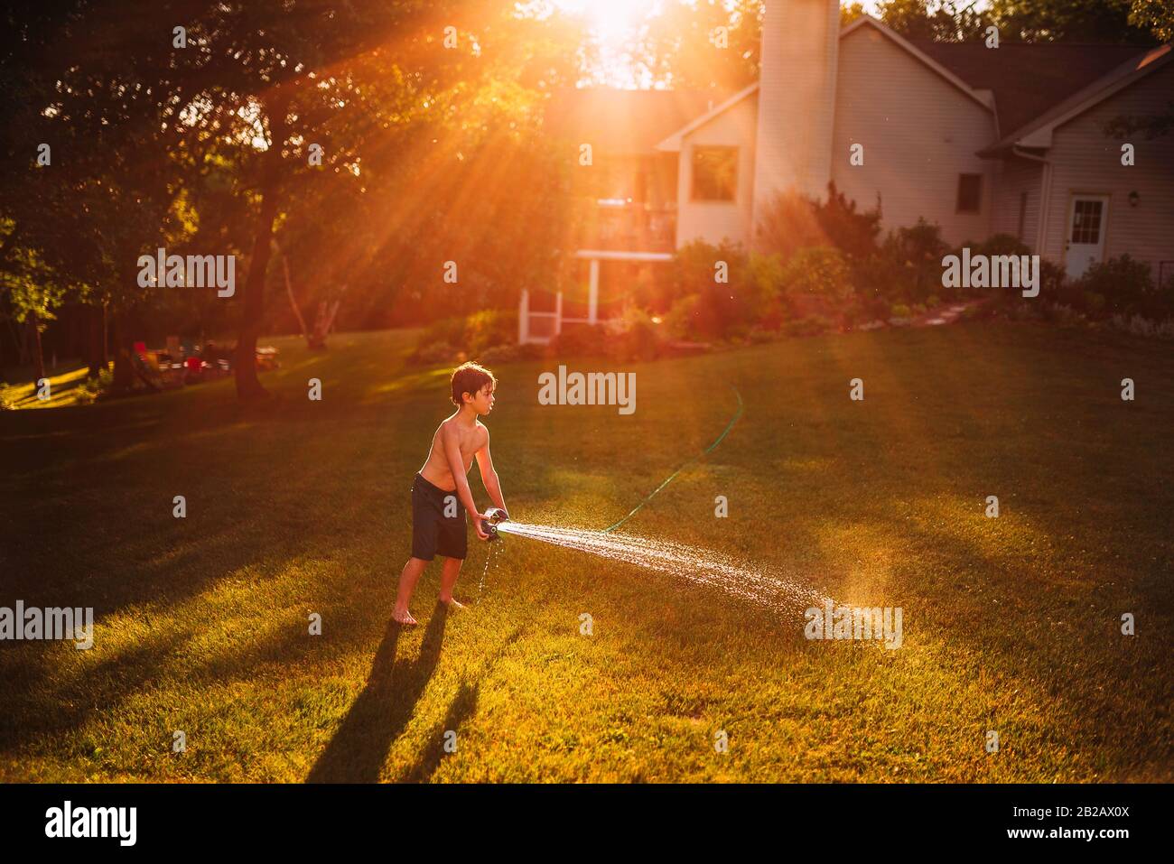 Boy standing in a garden playing with a water sprinkler, USA Stock Photo