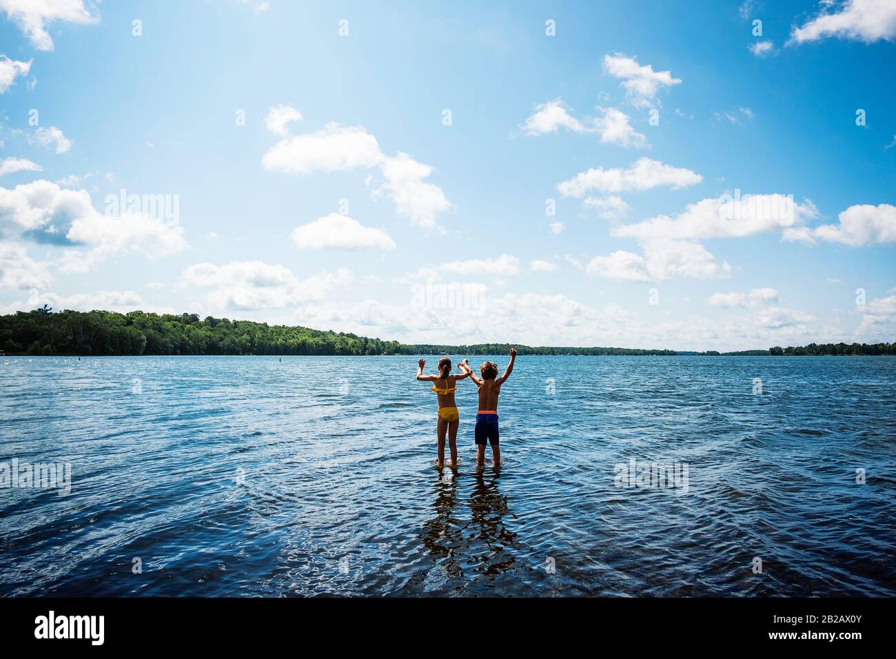 Rear view of two children standing in a lake with their arms raised, USA Stock Photo