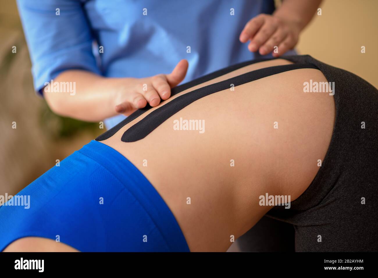 Physical therapist applying kinesio tape on female patient's lower back. Kinesiology, physical therapy, rehabilitation concept. Cropped shot close up. Stock Photo