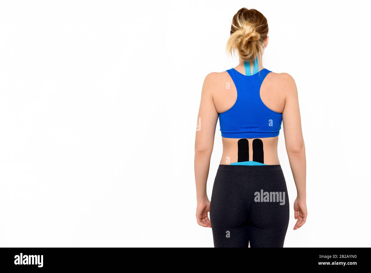 Rear view three quarter length studio shot of a female patient with kinesio tape on her neck and lower back, isolated over white background. Stock Photo