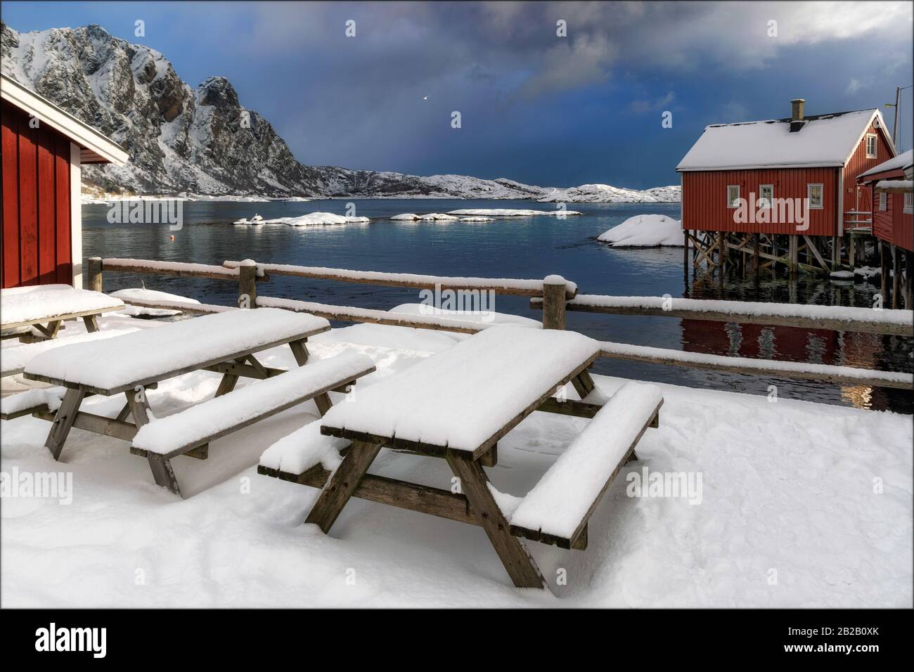 Snow covered picnic tables with benches with rorbuer cottages in Svolaer, Lofoten, Norway Stock Photo