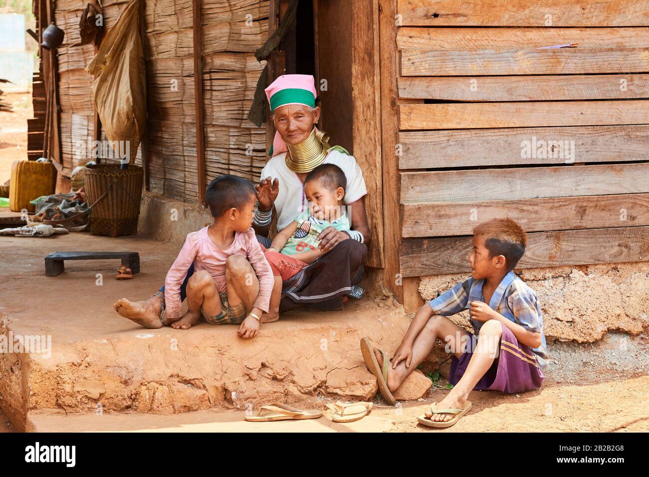 Kayan Lahwi woman with brass neck coils and traditional clothing looking at cellphone with her grandchildren. The Long Neck Kayan (also called Stock Photo