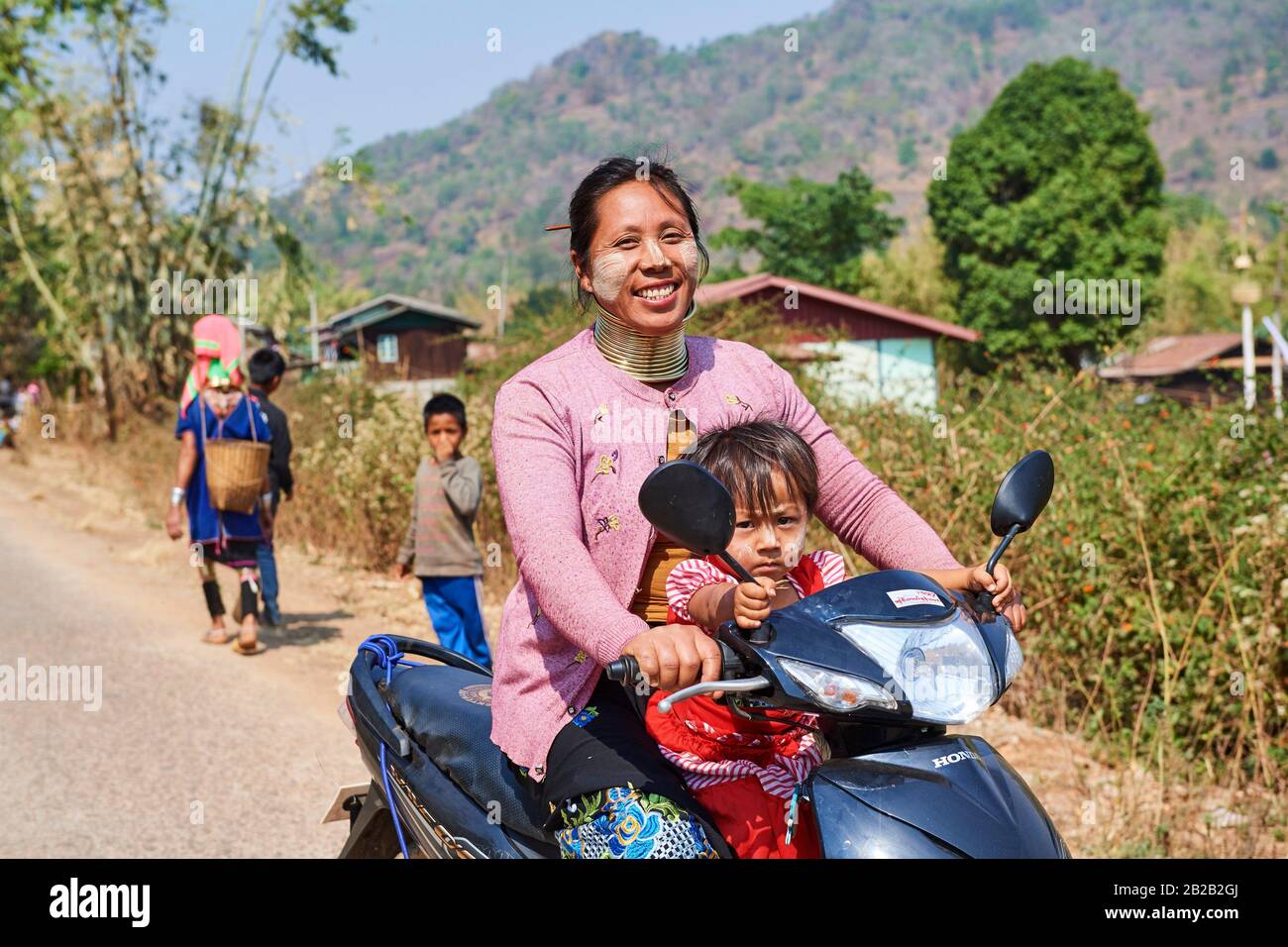 Kayan Lahwi woman with brass neck coils and traditional clothing riding a motorbike with her child. The Long Neck Kayan (also called Padaung in Stock Photo