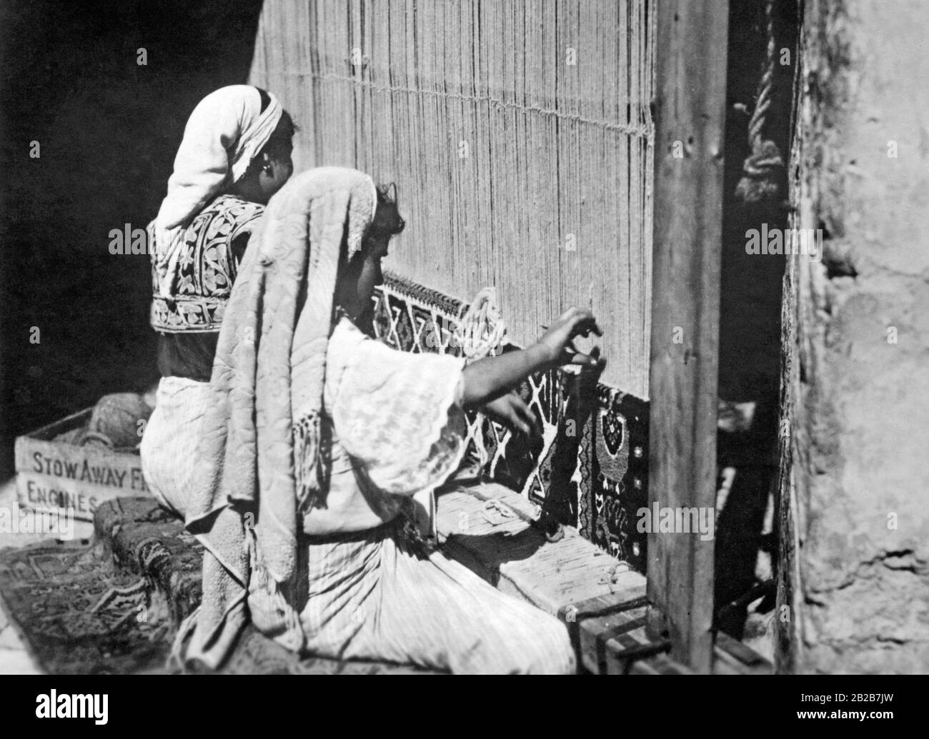 Tunisian women weaving carpets. The frame is fitted with bells so that one can hear when the women interrupt their work. Undated photo. Stock Photo