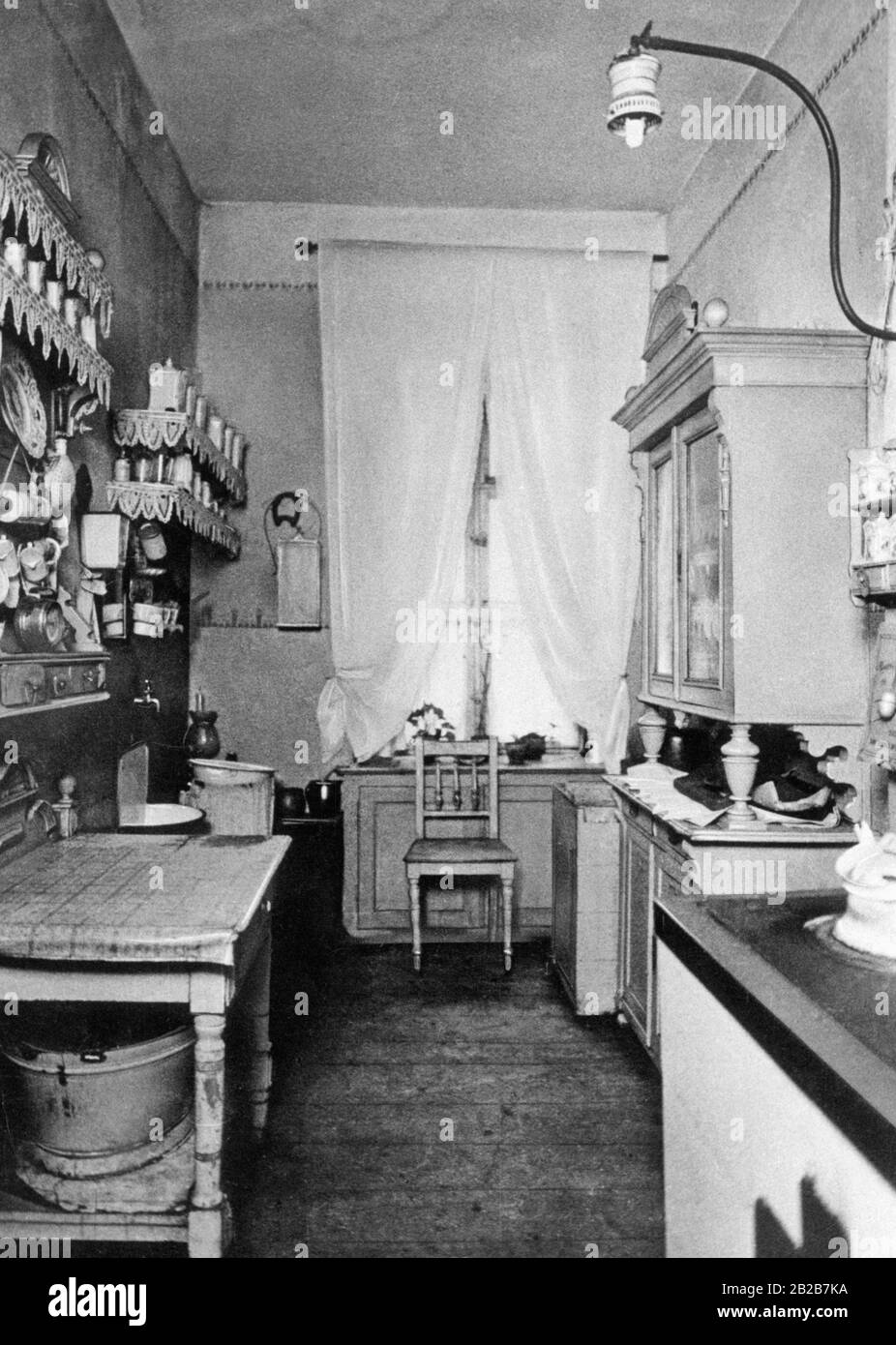 A typical middle-class kitchen at the beginning of the 20th century. In the foreground on the right the tiled kitchen stove, on the left behind the cast-iron 'sink'. Under the gas lamp as reserve lighting there is an oil lamp. The washtub under the kitchen table and the shell tops of the buffet, table and shelf with the scalloped edge papers clearly mark the age of this kitchen. Stock Photo