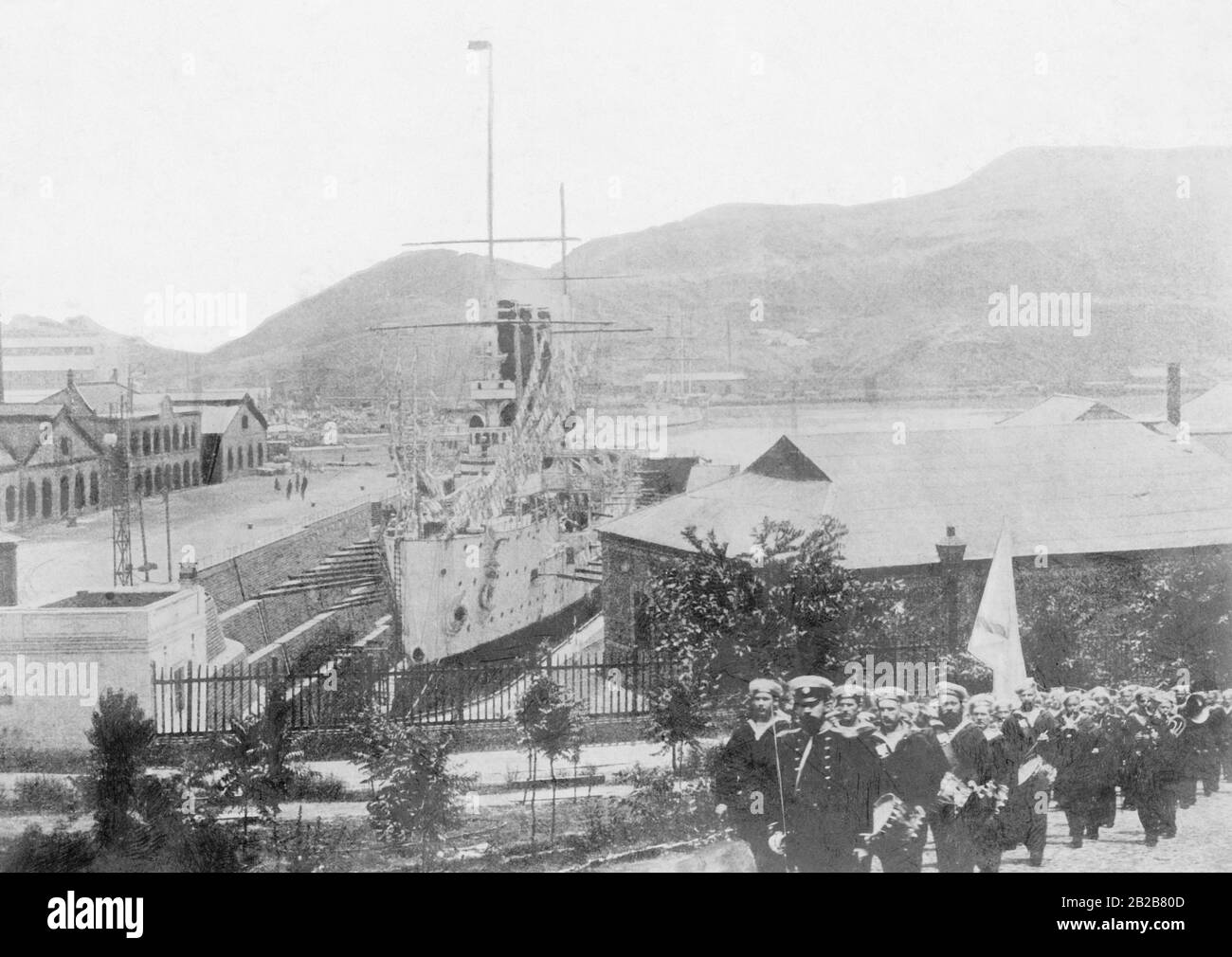 View to Port Arthur, today's Lüshunkou, a russian battleship in the dry dock and a marching band passing by. Stock Photo