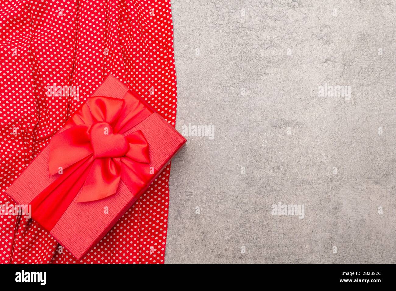 Romantic gift concept. Red box with bow and polka dot cloth. On a stone ...