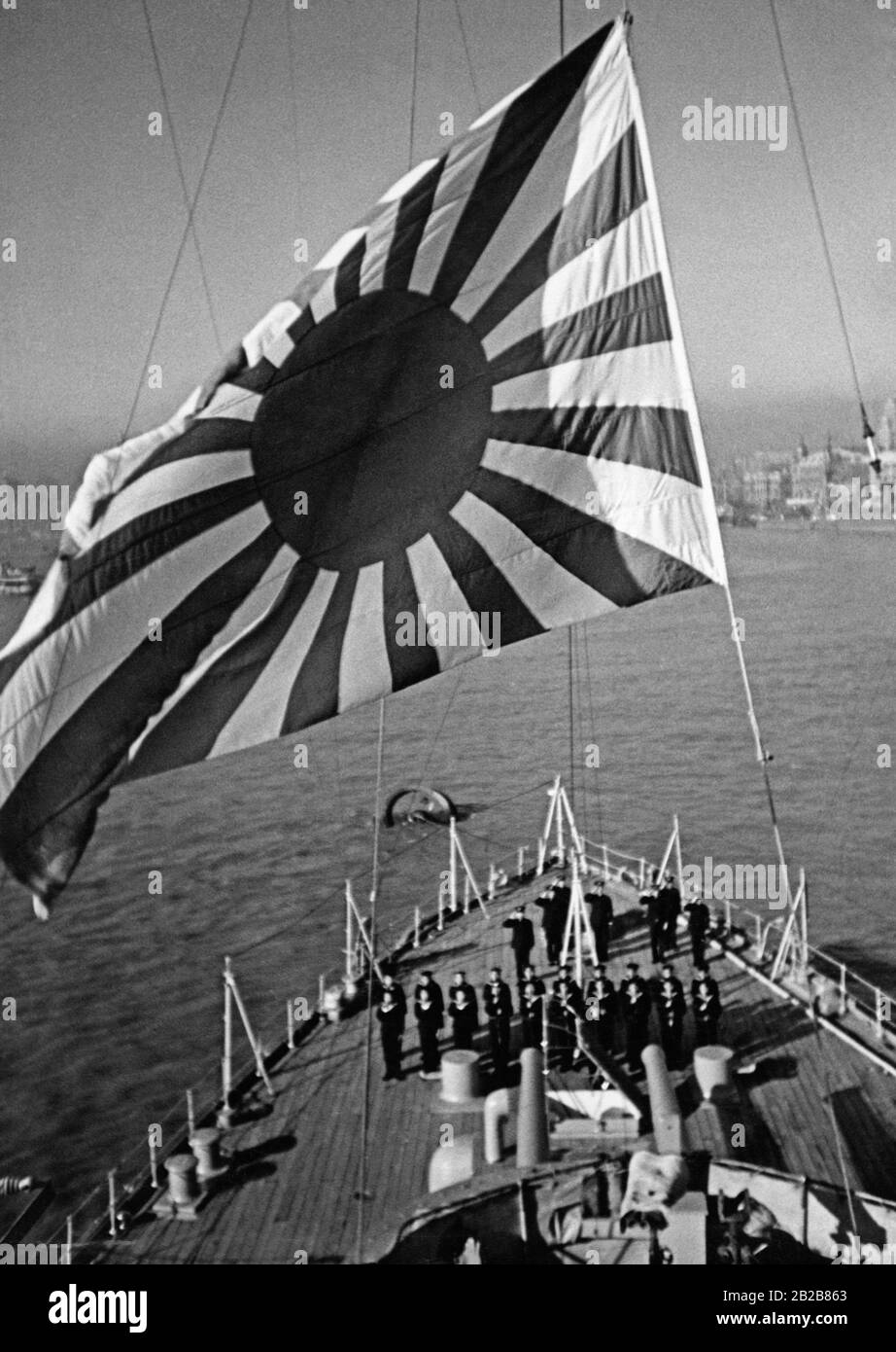 The flag of the Imperial Japanese Navy is hoisted on board the Japanese flagship Izumo. Below the flag there are saluting sailors. Stock Photo