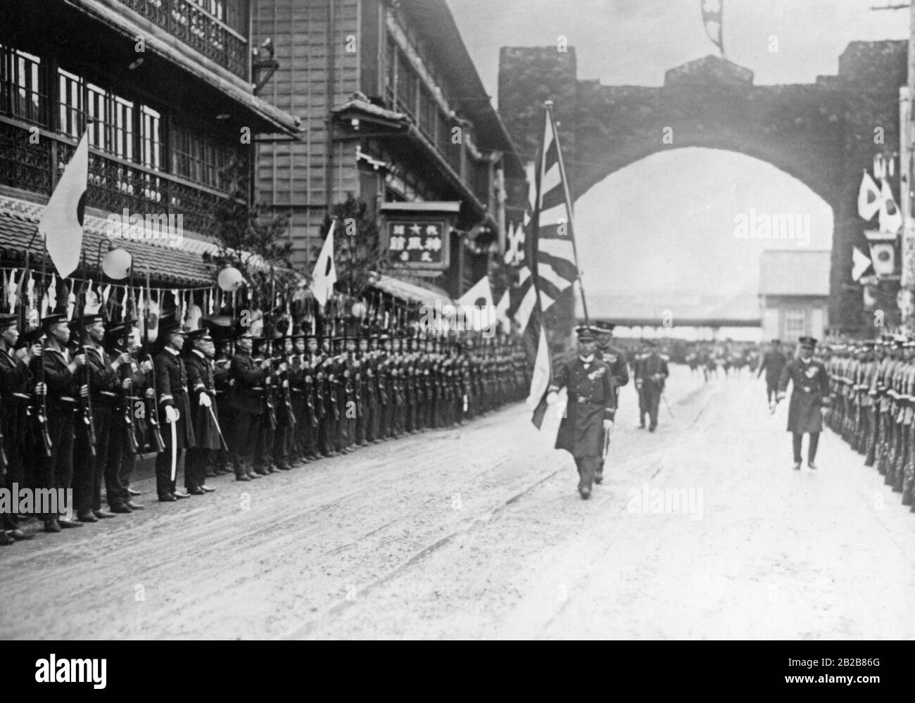 The Japanese Emperor Hirohito is welcomed in the city of Yamada. The street from the station is lined with soldiers and sailors. Flag bearers march in the street. Stock Photo
