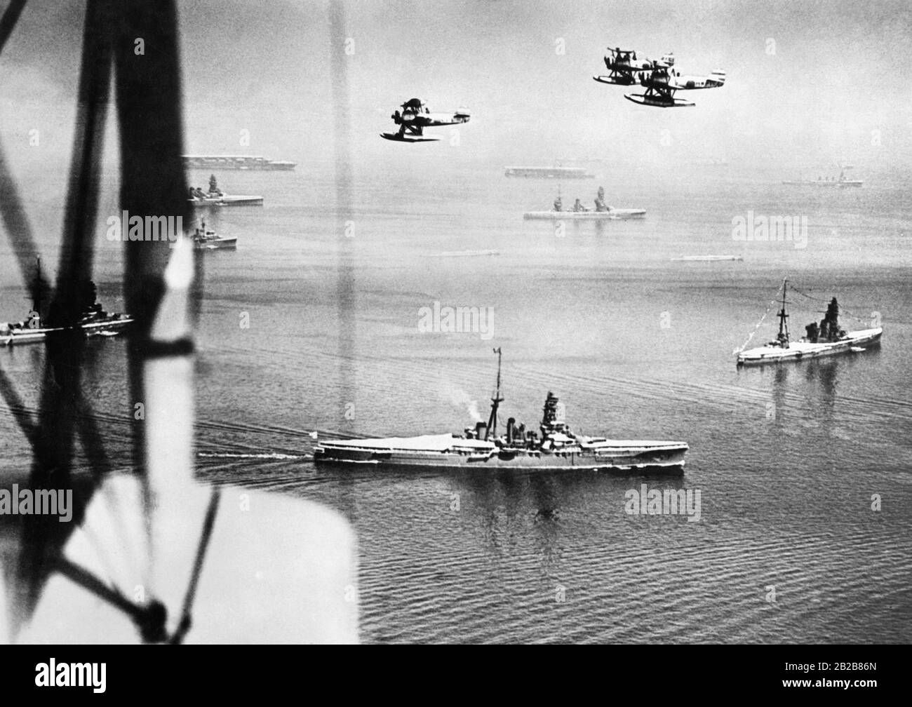 View over the sea near Yokohama in Japan during a parade of the Imperial Japanese Navy on August 28, 1939. In the foreground are some destroyers of the Navy as well as airplanes flying above. In the background in the fog are two aircraft carriers. Stock Photo