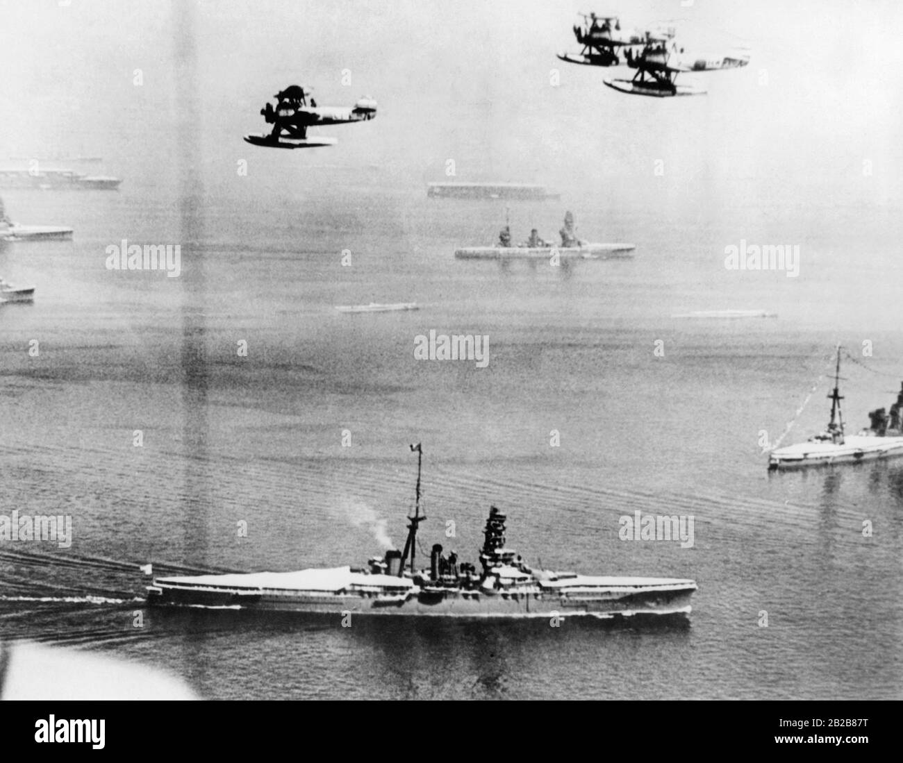 View over the sea near Yokohama in Japan during a parade of the Imperial Japanese Navy on August 28, 1939. In the foreground are several destroyers of the Navy as well as airplanes flying above. In the background in the fog are two aircraft carriers. Stock Photo