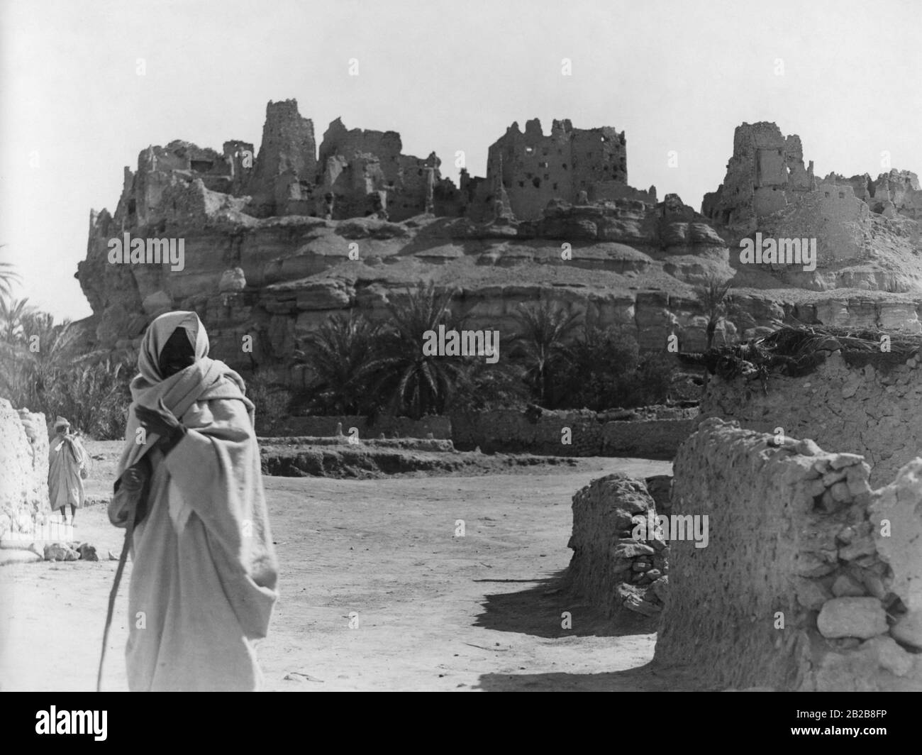 A man in traditional jellabiya stands before the ruins of the once magnificent fortress of a Berber castle. Stock Photo
