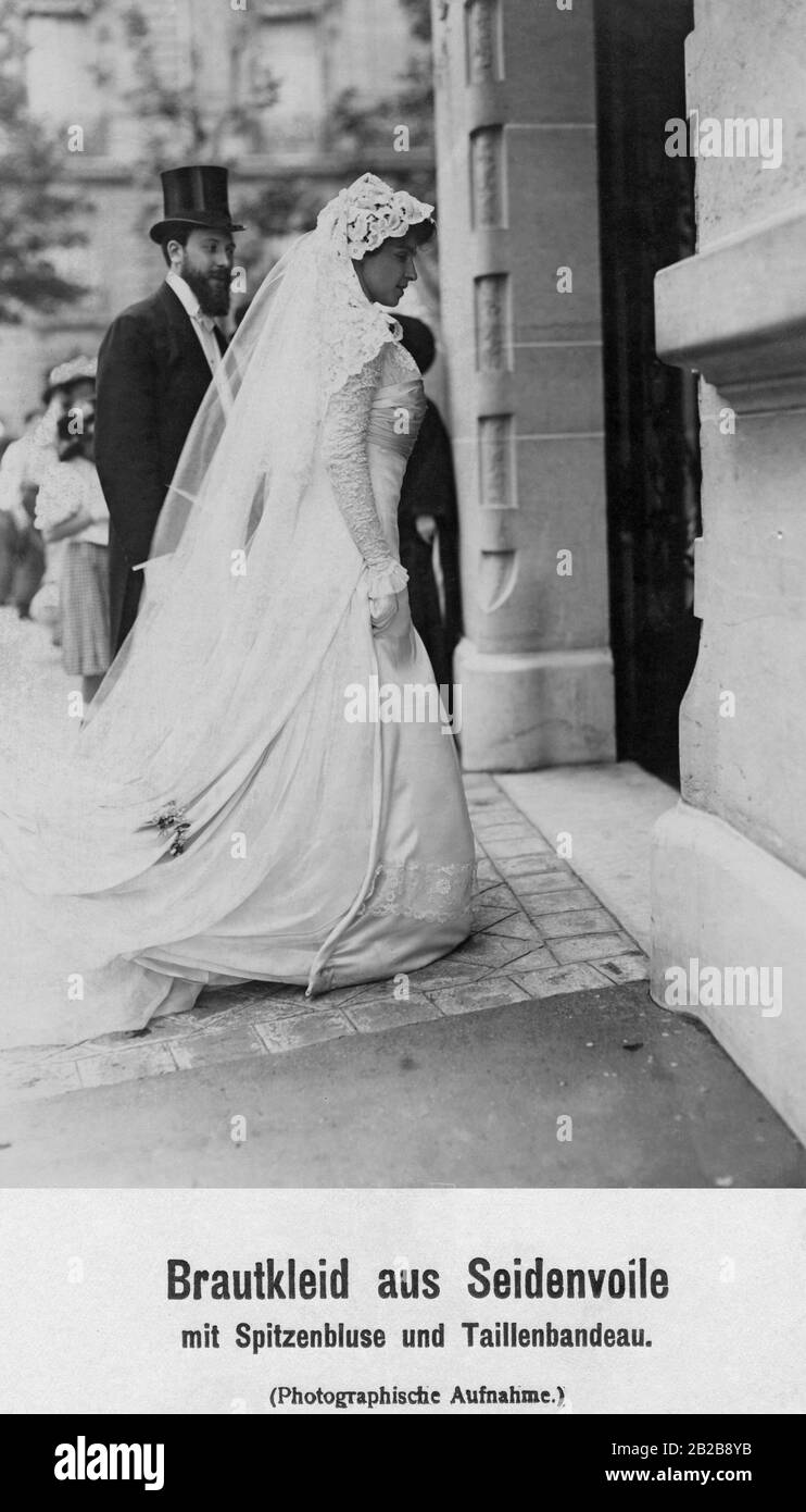 A bridal couple enters the church. The bride wears an elaborate dress made of silk voile with lace blouse and waist band. Stock Photo