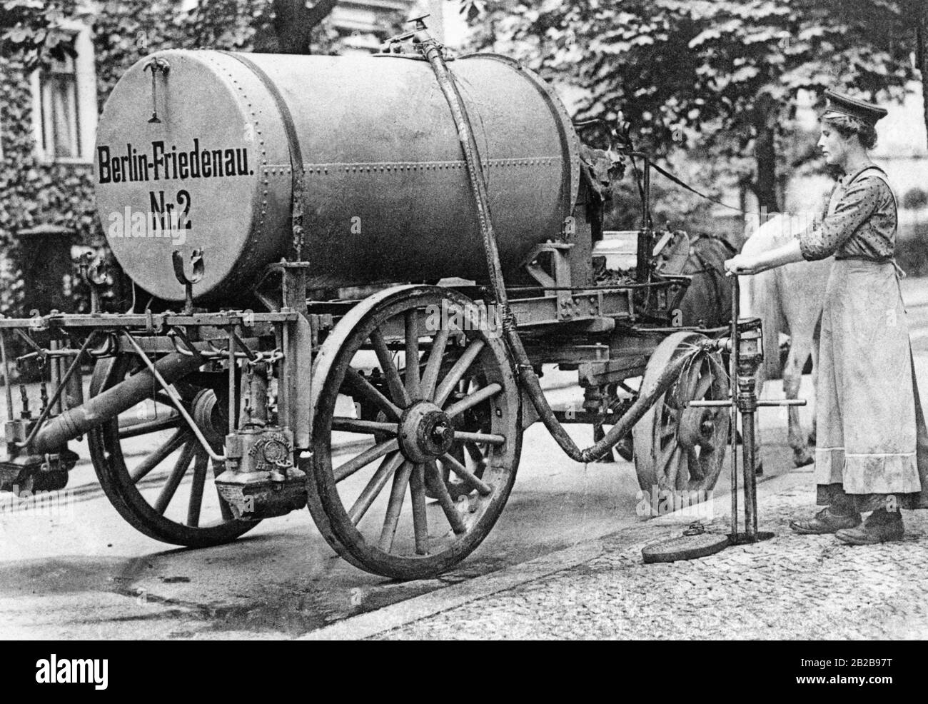 In the third year of the war, the shortage of male workers had become so serious that the Berlin City Administration also decided to employ female helpers for street cleaning. The picture shows one of the first female street cleaners pouring water into the tank car used at that time. Stock Photo