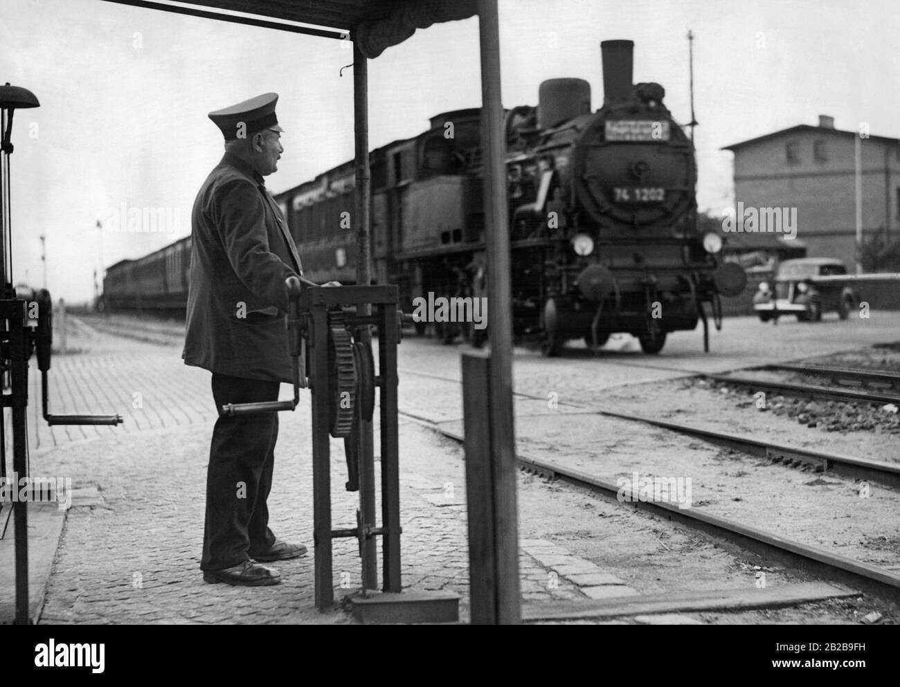 A crossing keeper of the Deutsche Reichsbahn (German Reich Railway) at a barrier installation next to a passing train. Stock Photo