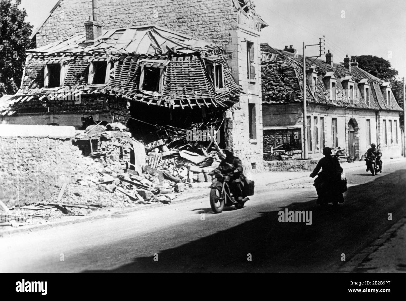Advance between Paris and Compiegne in France. In the background in the rubble of a destroyed house. Soldiers are riding their motorcycles on the road. Stock Photo