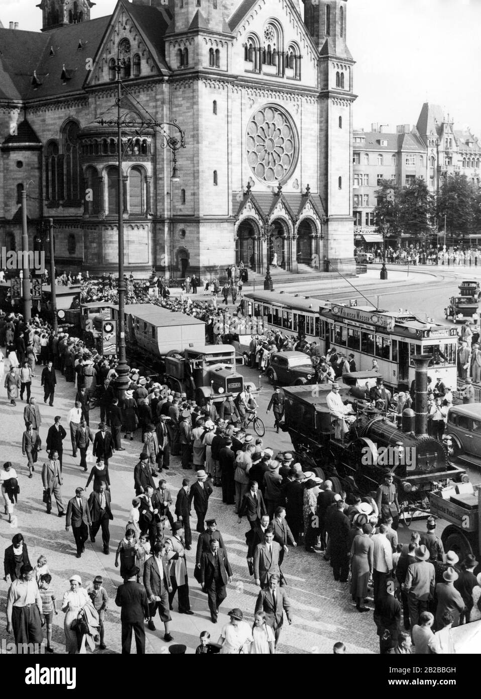 The replica of the first German locomotive, the 'Adler', rides through Berlin. It passes the Kaiser Wilhelm Memorial Church and will be on display at the exhibition 'Deutschland' in the Exhibition Halls on Kaiserdamm. Many people line the roadside and wave to the locomotive. A tram runs in the background. Stock Photo