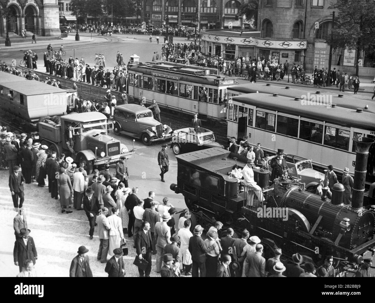 The first German locomotive 'Adler' is transported through Berlin to the exhibition halls at Kaiserdamm. The convoy passes the Kaiser Wilhelm Memorial Church. It is accompanied by SS men. Stock Photo