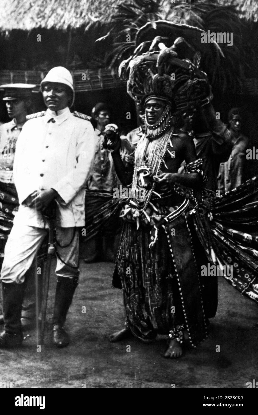 The king of Bamum in German uniform in the German colony of Kamerun. A servant of the king of Cameroon wears the king's stately dance costume. Natives stand in European clothes and some even in German uniform in the background. Undated picture. Stock Photo