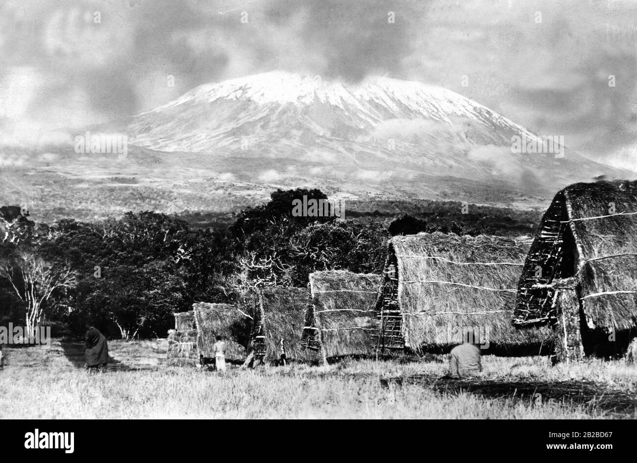 Straw huts in front of a snowy mountain in German East Africa, probably a summit of Kilimanjaro. Undated photo. Stock Photo