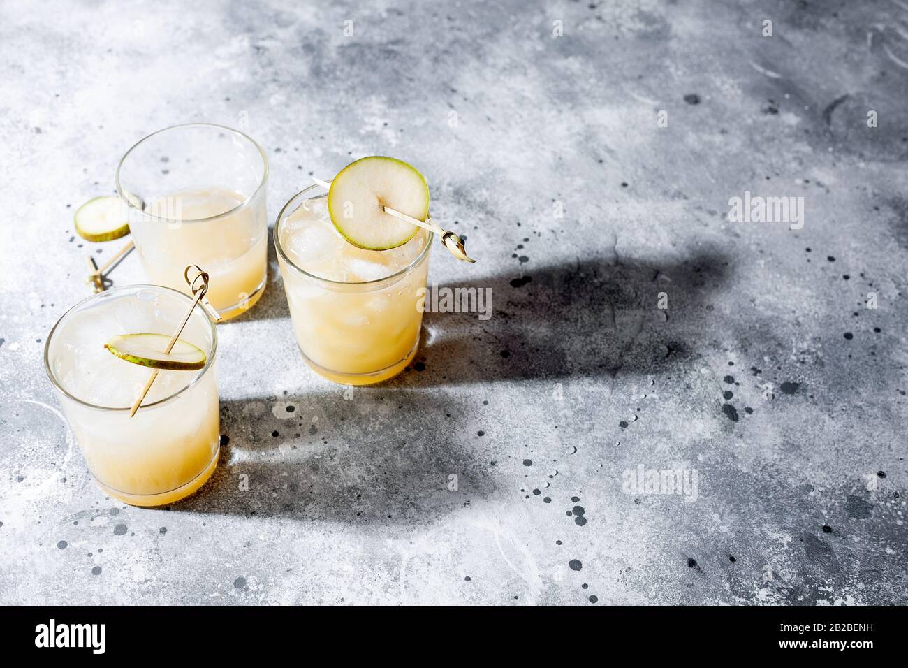 Cold pear cocktail or mocktail with soda and pear puree and fruit slices in short glass on gray background with shadow. Refreshing summer drink Stock Photo
