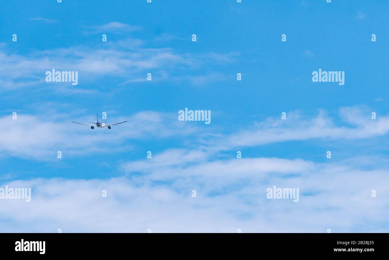 Commercial airline flying on blue sky and white fluffy clouds. Airplane flying on sunny day. Rear view of international flight passenger plane. Summer Stock Photo