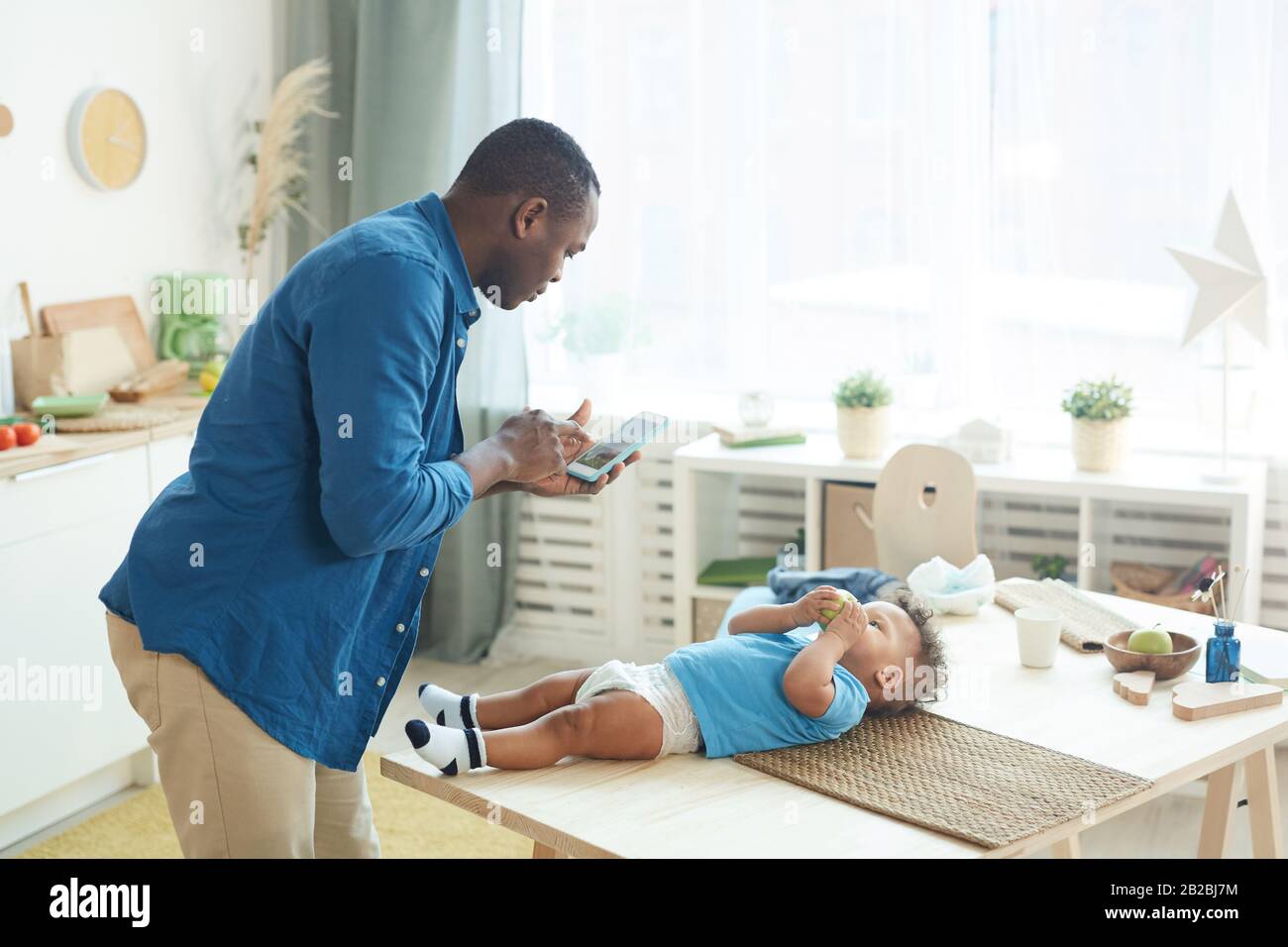 Side view portrait of mature African man calling wife while caring for baby in home interior, copy space Stock Photo