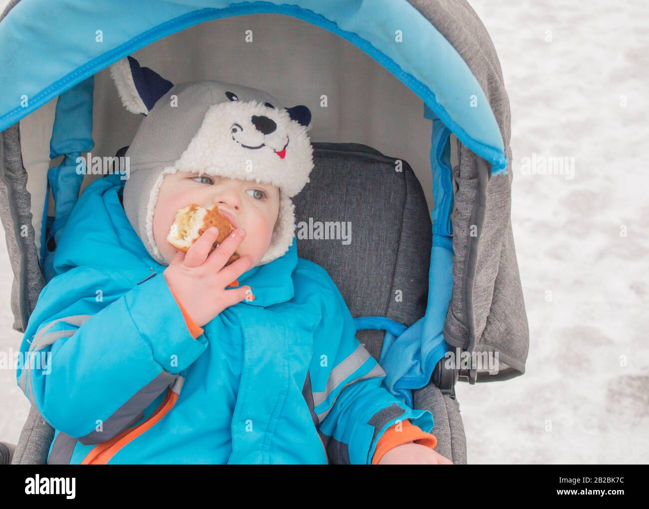 little boy sitting in the stroller in the winter and eats cake Stock Photo