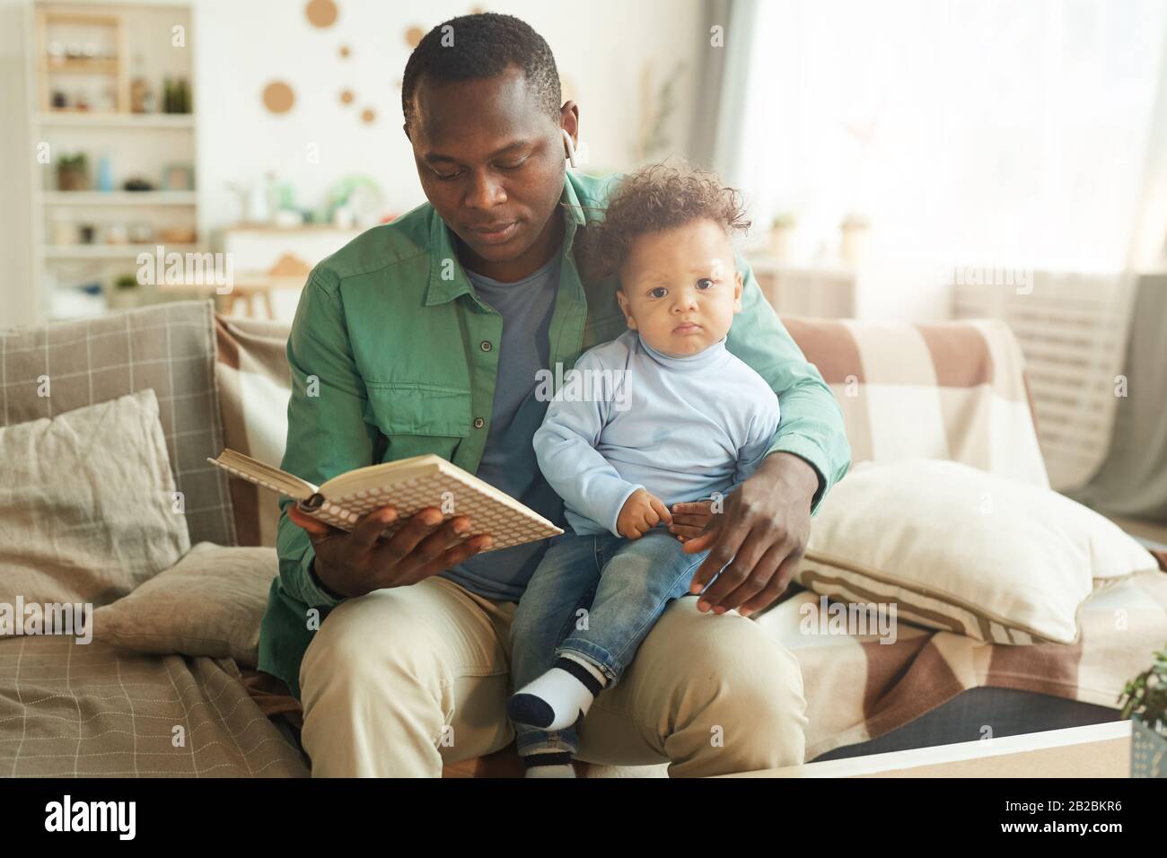 Portrait of mature African-American man reading book to child sitting on fathers lap, copy space Stock Photo