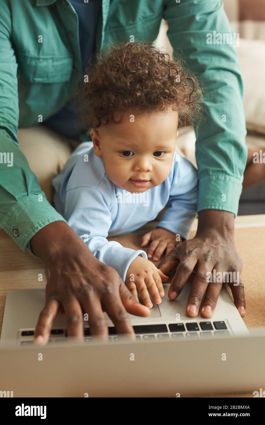 Vertical portrait of cute AfricanAmerican baby using laptop and