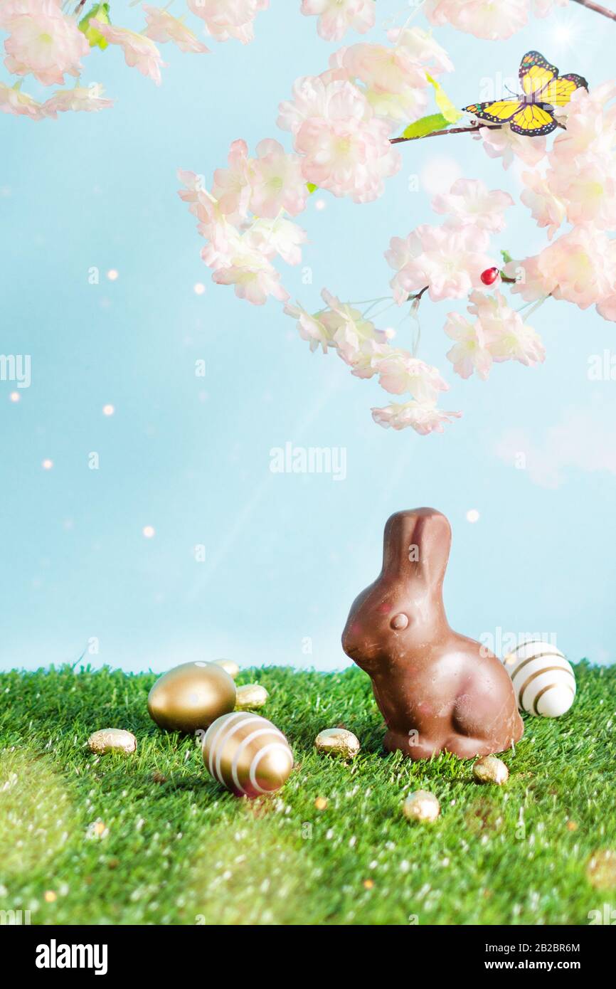 Easter colored eggs, chocolate Easter bunny and blooming spring tree branches over blue background. Happy Easter time. Easter greeting card background Stock Photo