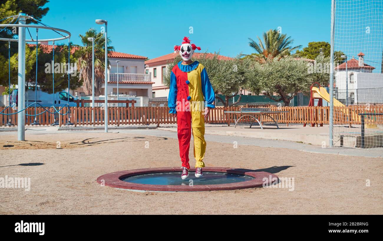 a scary clown wearing a colorful yellow, red and blue costume, bouncing
