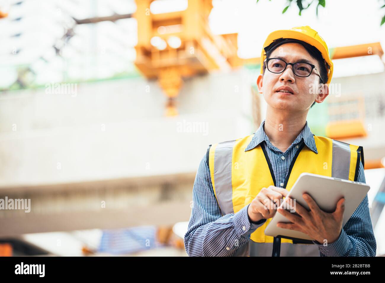 Image outside the industrial construction engineers in yellow protective helmet discuss new project while using laptop and happy smile on the open bui Stock Photo