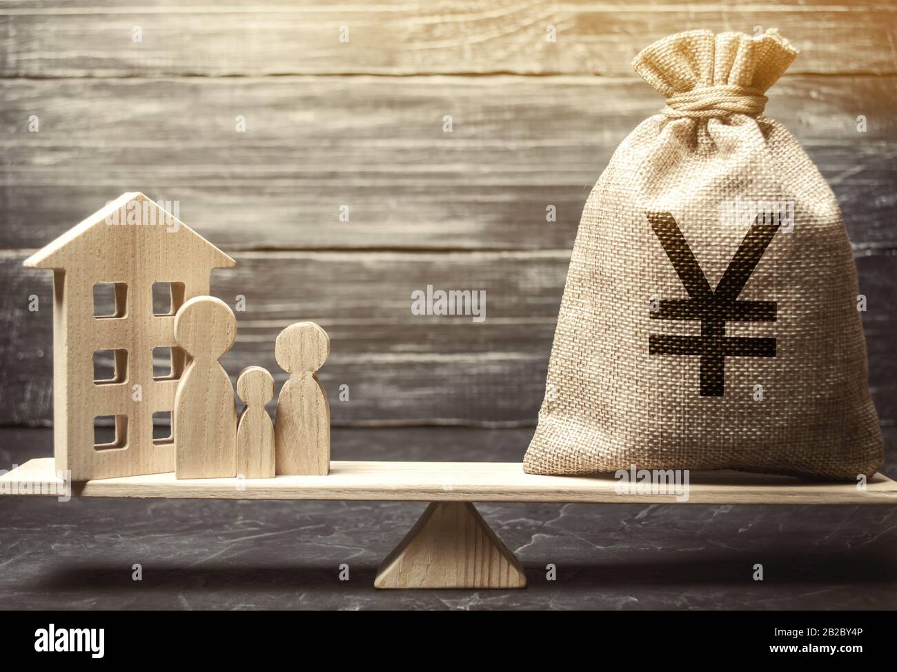 Money bag with yen / yuan and wooden house on scales with family. Fair value of real estate and housing. Payment of the mortgage interest rates. Redem Stock Photo