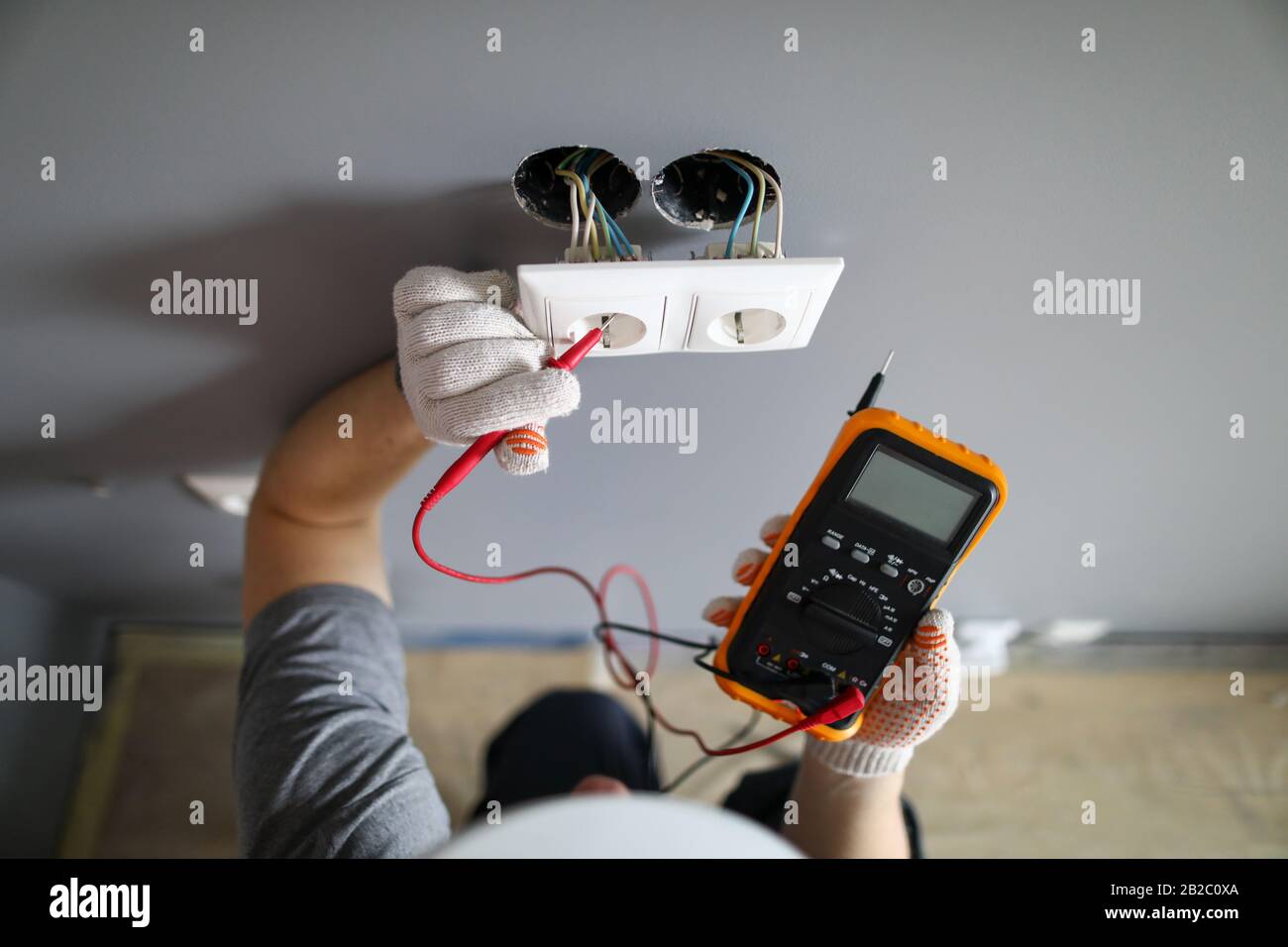 Man in hard hat and protective gloves checking wal outlet with tester Stock Photo