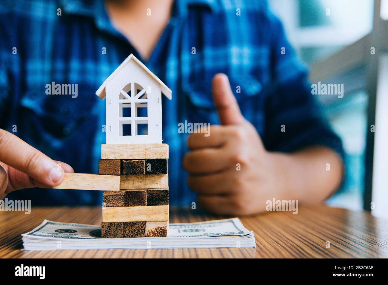 Hand holding a piece of wood block with model white house on dollar banknote. Insurance and property investment real estate concept. Stock Photo