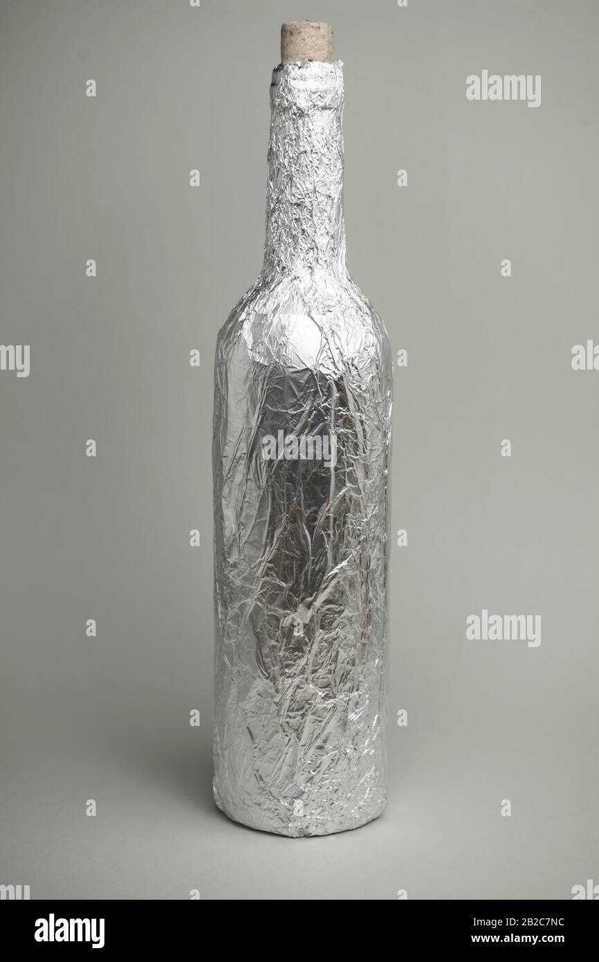 Bottle of wine wrapped in foil on a dark glass table gray background