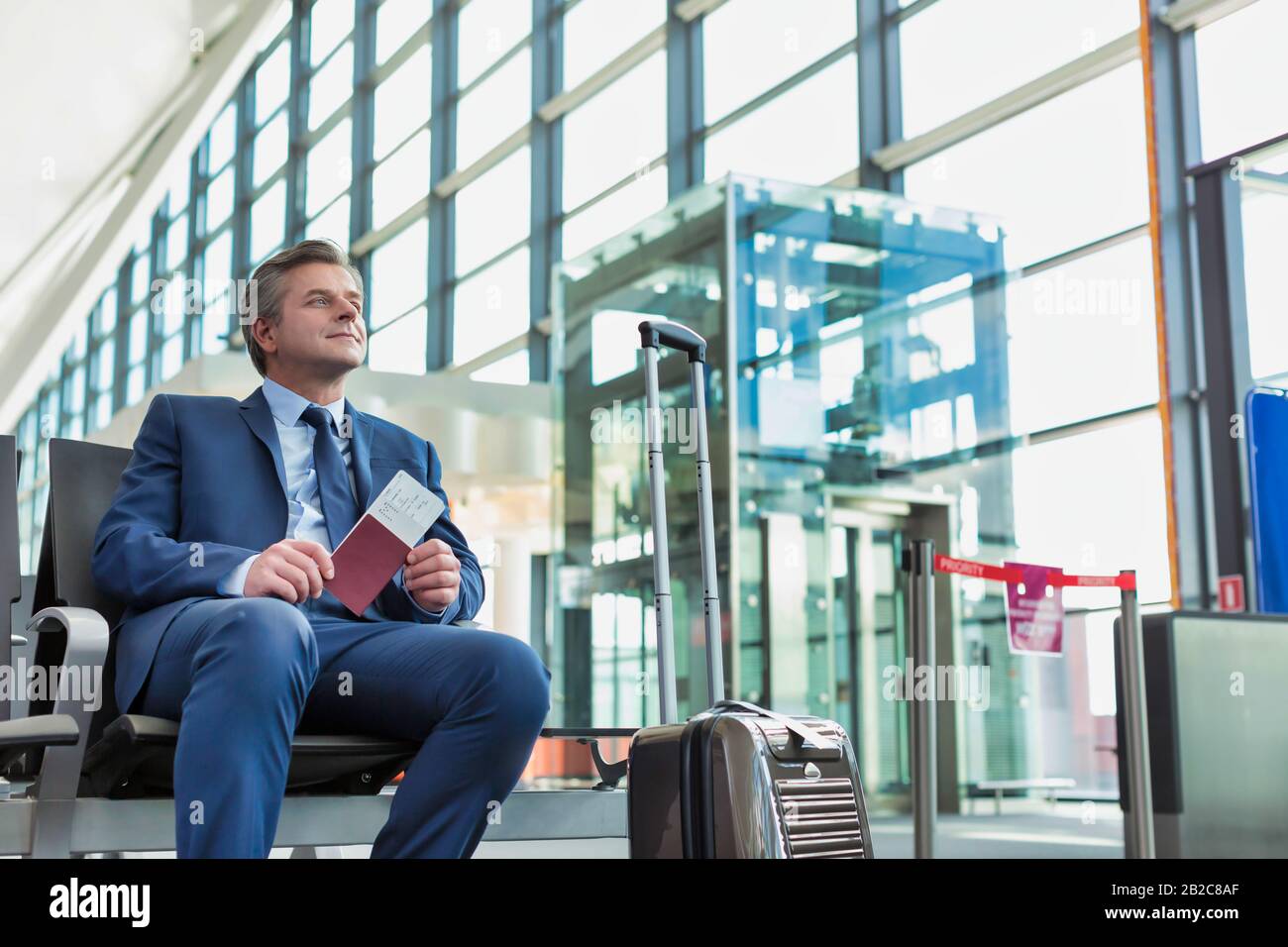 Portrait of Mature businessman sitting and holding his passport while waiting in gate for boarding at airport Stock Photo