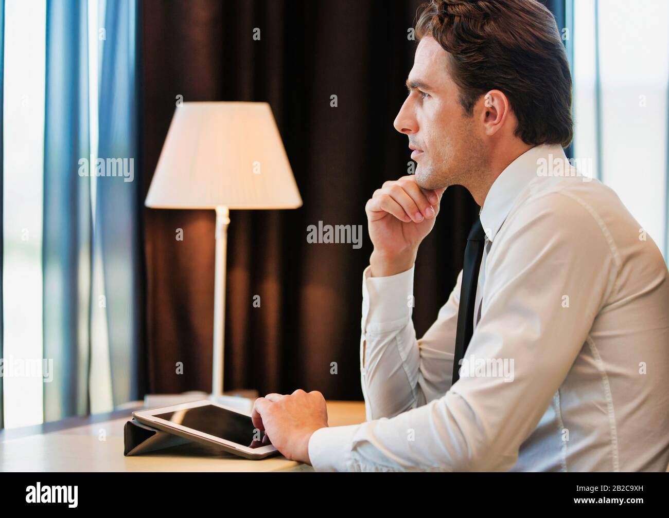 Thoughtful businessman using digital tablet while sitting with lens flare Stock Photo