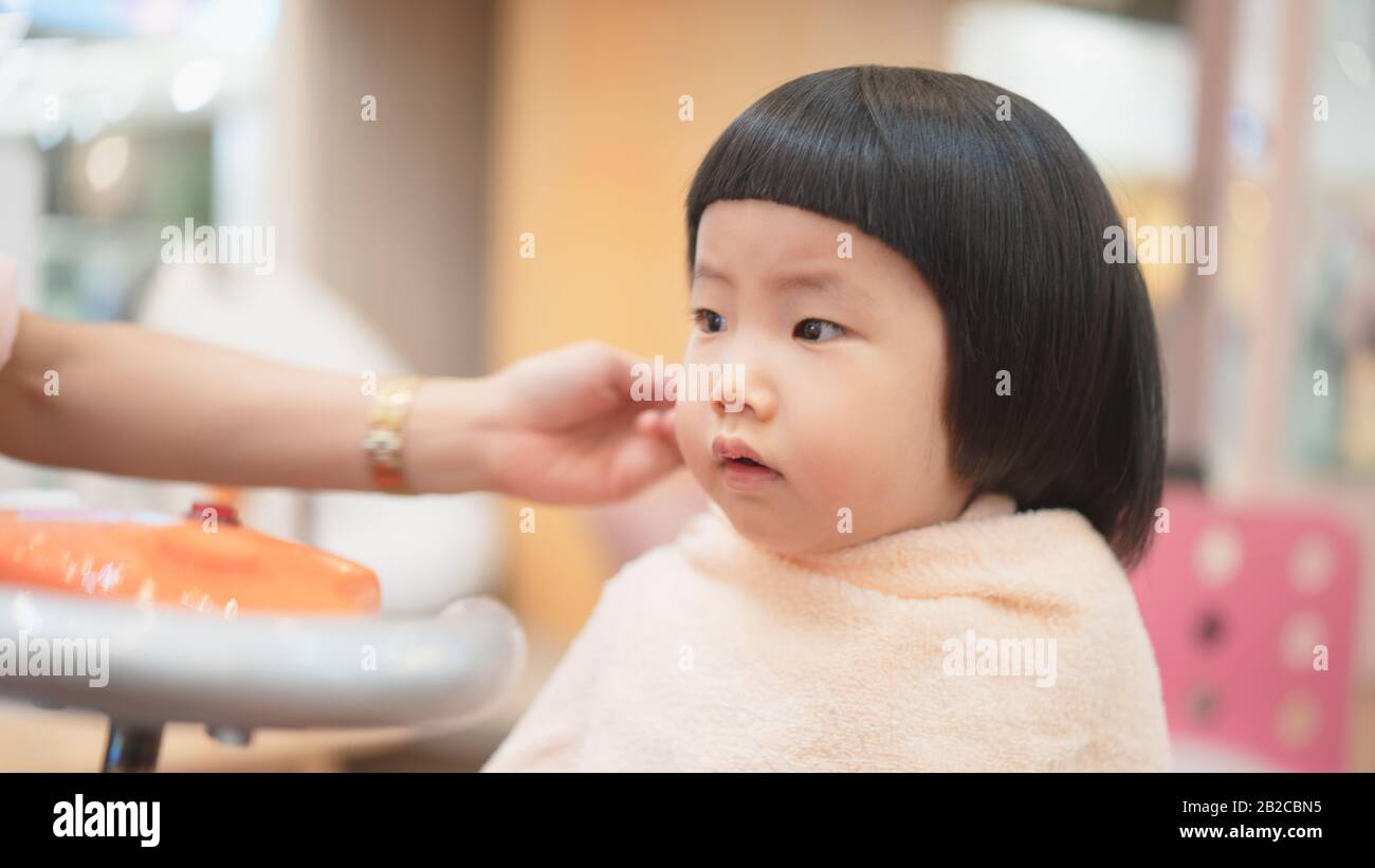 Adorable Asian toddler in baby salon shop with stunning face when looking  bang hairstyle in the mirror while get hair trimming after dry her hair. Ba  Stock Photo - Alamy