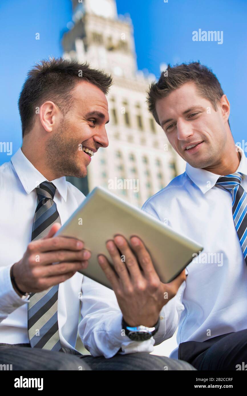 Portrait of handsome businessman showing business plan to the other businessman over digital tablet while sitting Stock Photo