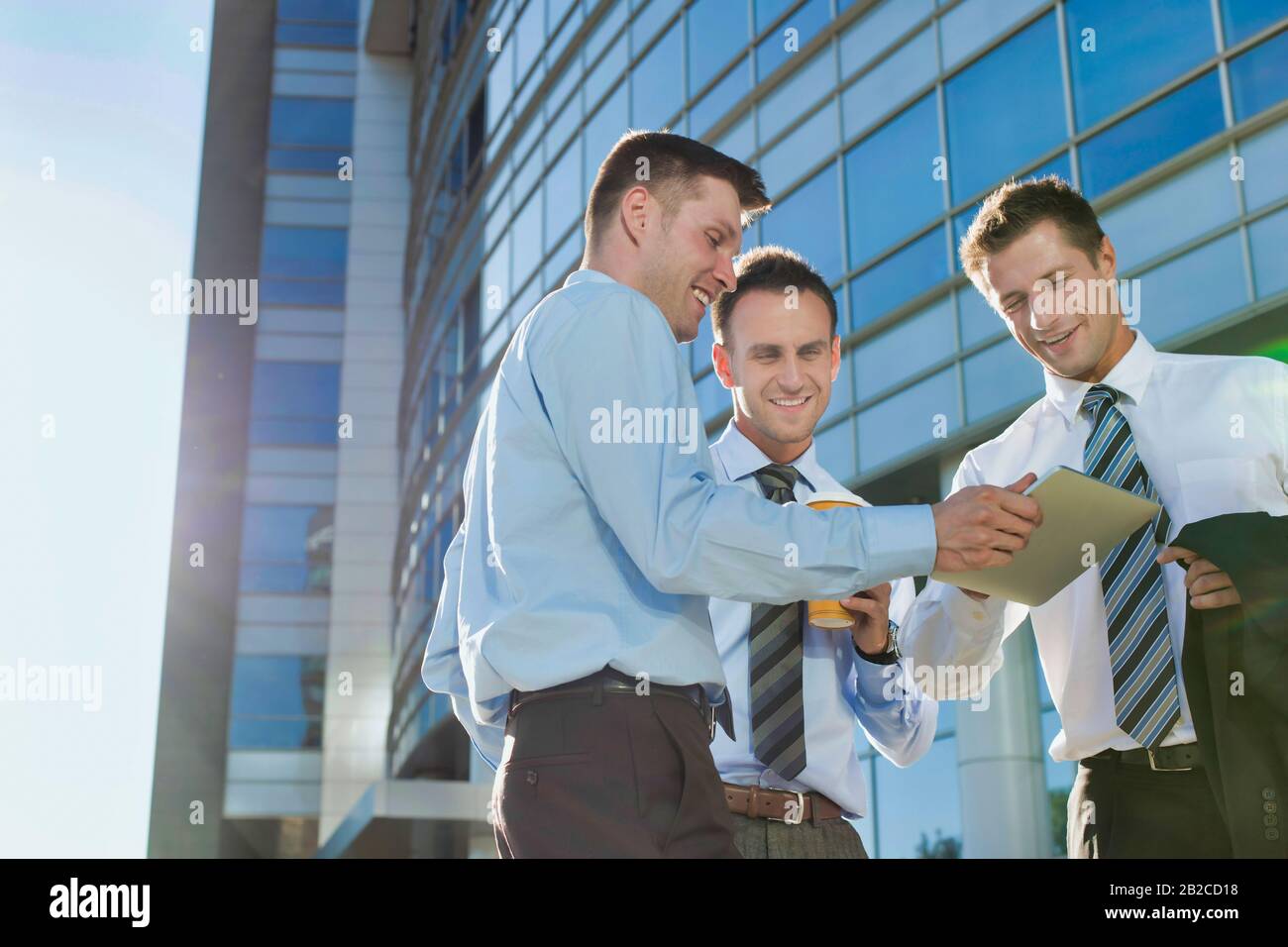 Mature attractive businessman showing and discussing plans over digital tablet with colleagues against office building Stock Photo