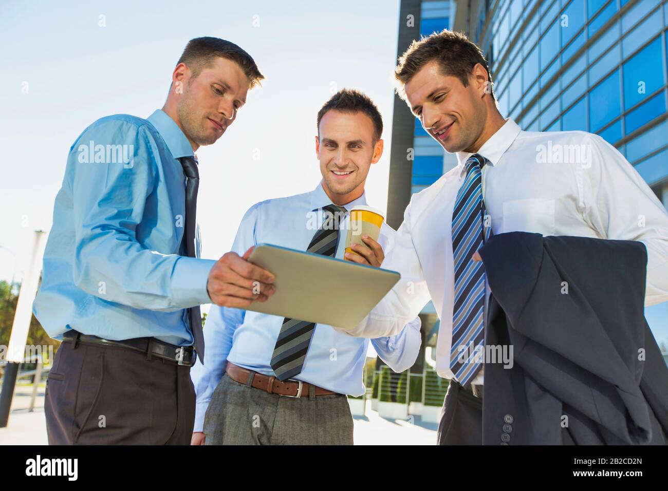 Mature attractive businessman showing and discussing plans over digital tablet with colleagues against office building Stock Photo