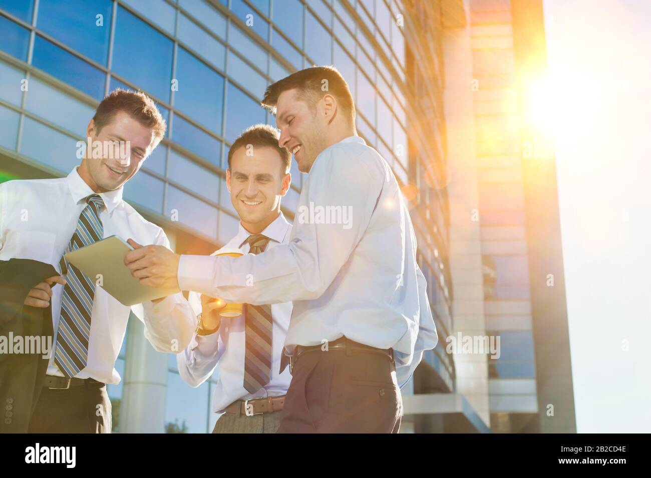 Mature attractive businessman showing and discussing plans over digital tablet with colleagues against office building Stock Photo