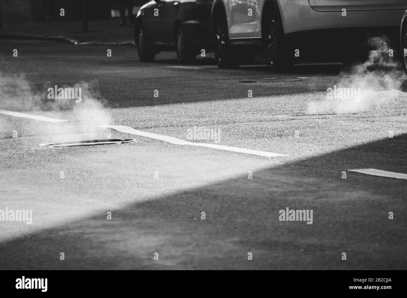 Steam going out of manholes on street road in early morning Stock Photo