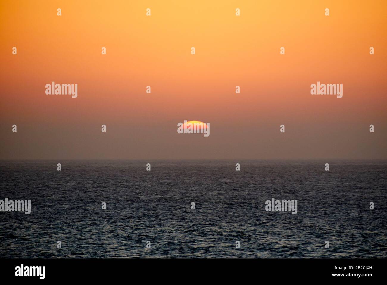 red sun setting in the evening with red sky from saharan dust blown in by the calima wind from africa Lanzarote canary islands spain Stock Photo