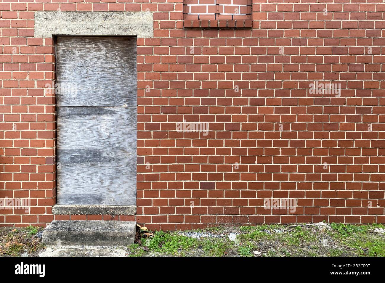 a boarded up door way on an abandoned red brick back alley warehouse building Stock Photo