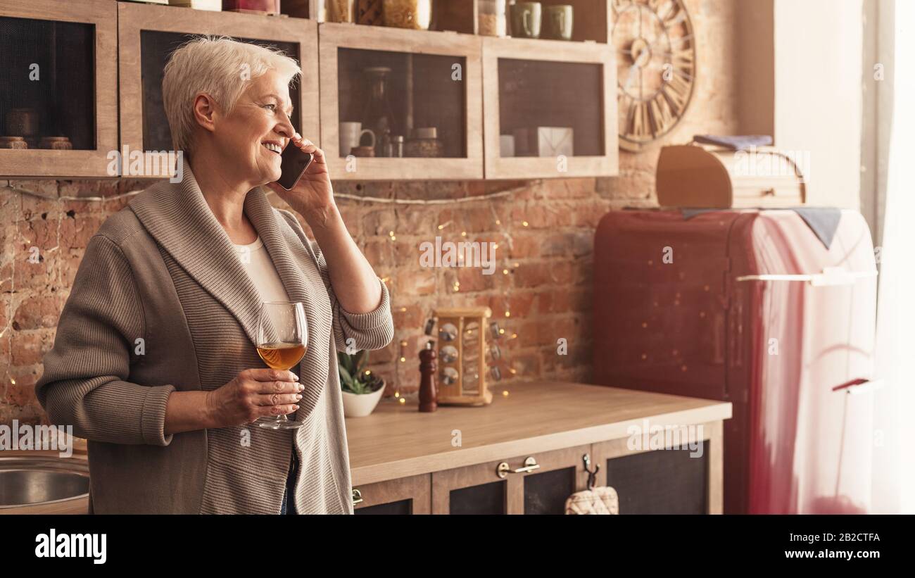Happy senior woman enjoying glass of wine while talking on cellphone Stock Photo