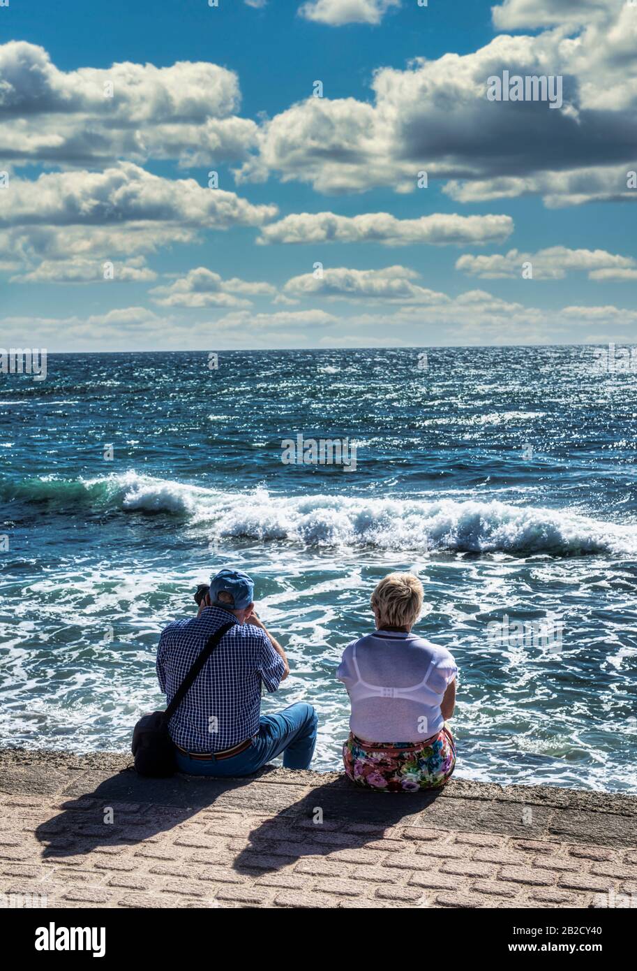 Elderly couple sitting and watching the waves Stock Photo